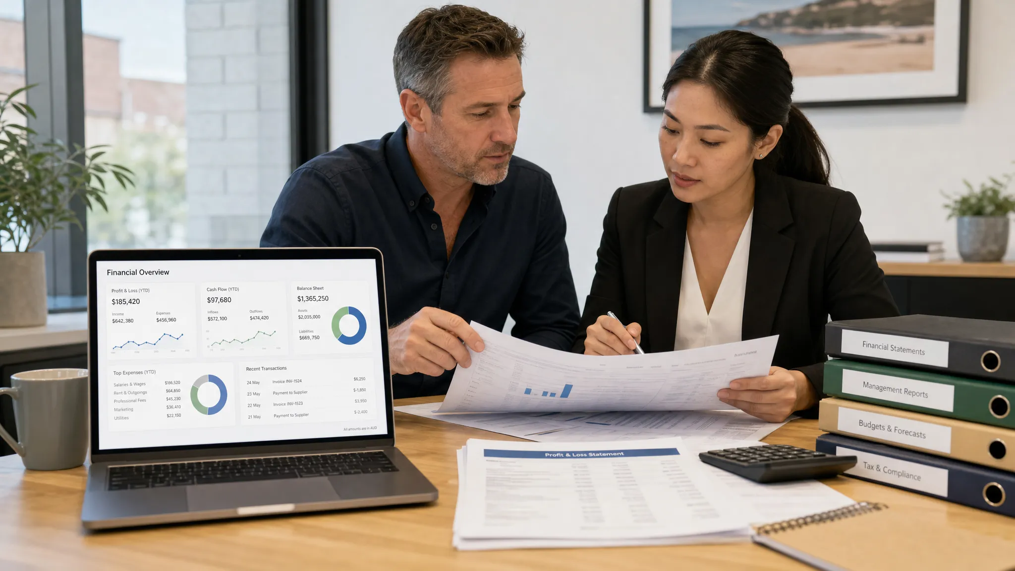 An Australian business owner and senior accountant reviewing printed financial reports at a meeting table, with a laptop facing the camera showing a simple financial dashboard and organised folders beside the documents.