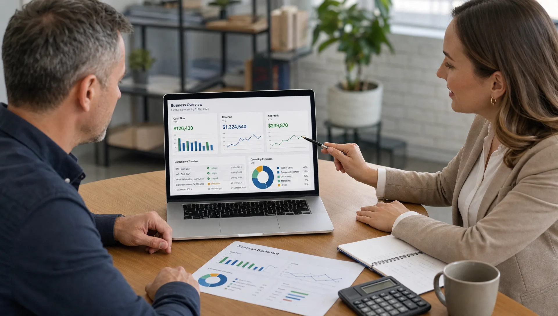 A business owner and accounting adviser reviewing financial reports on a laptop and printed dashboard, with visible charts showing cash flow, revenue and compliance timelines. The laptop screen faces the viewer correctly and no content appears behind the screen.