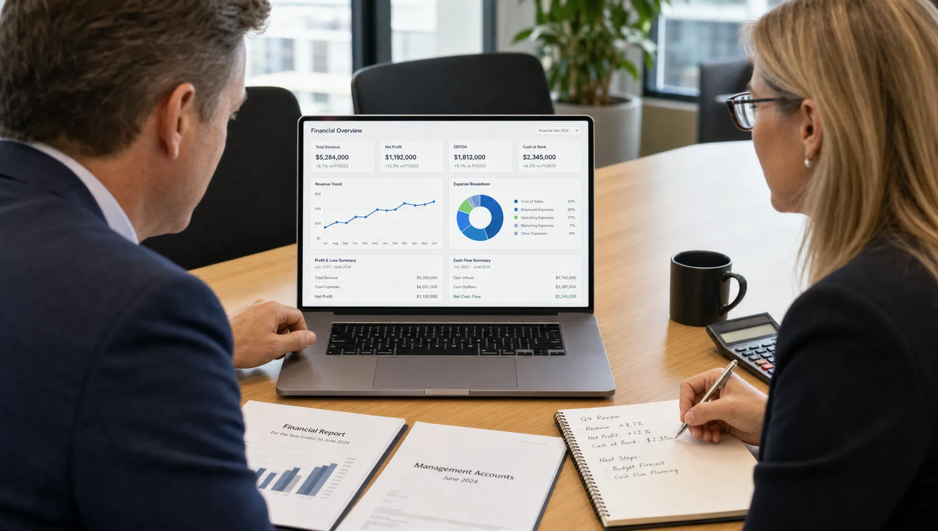 An Australian business director and accountant reviewing a clean financial reporting dashboard on a laptop facing them, with charts on the screen oriented correctly and financial documents neatly arranged on a meeting table.