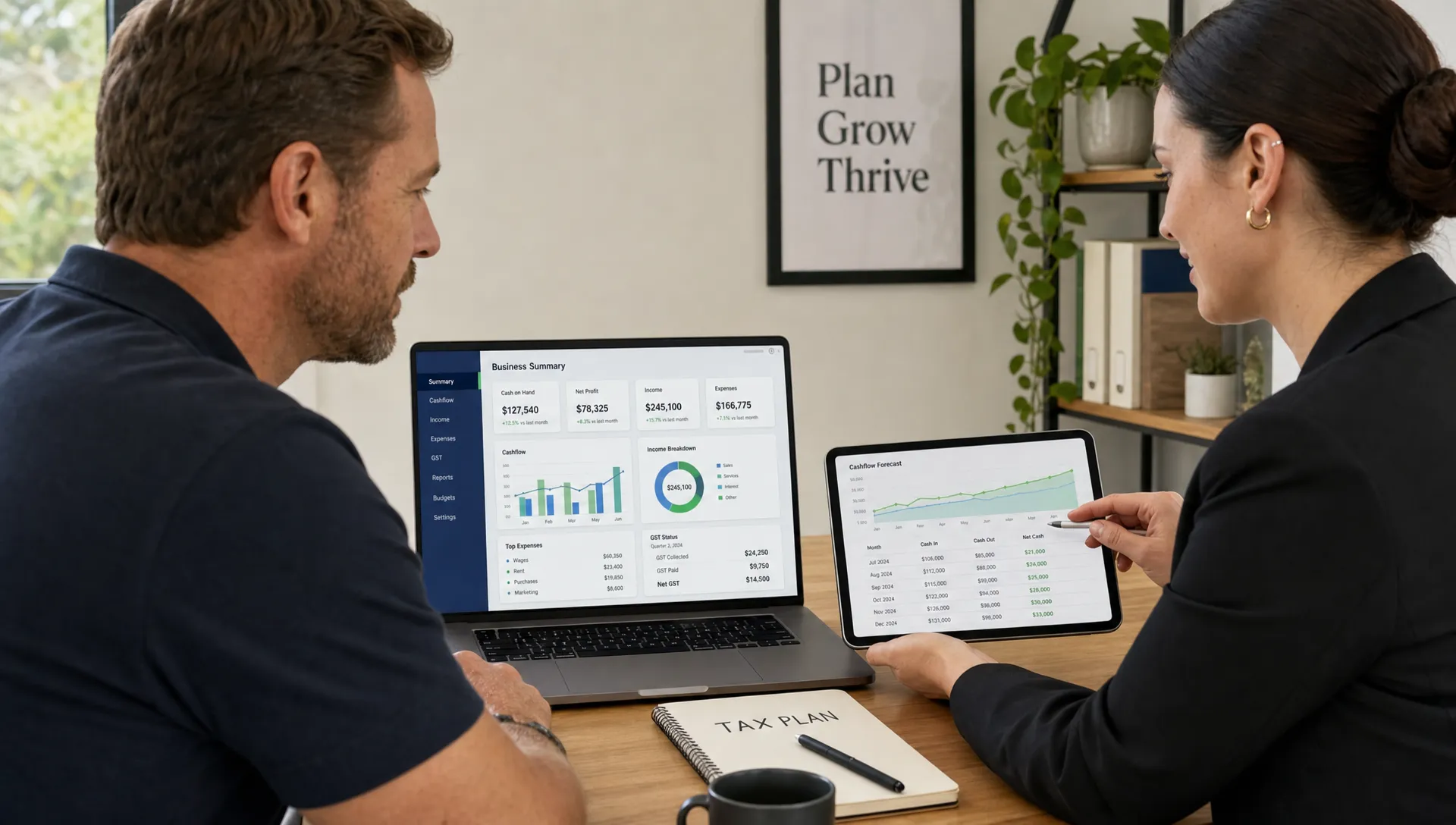 An Australian business owner and tax accountant review financial dashboards on a laptop and tablet during a consultation.