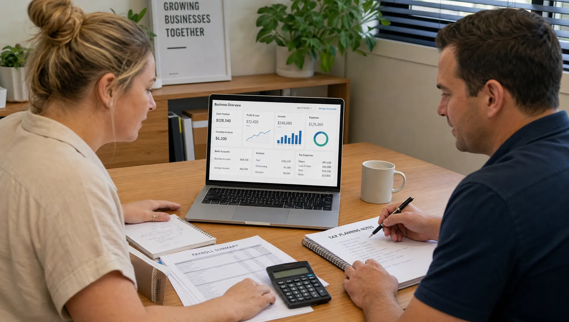 An Australian small business owner and accountant reviewing organised financial records, payroll summaries and tax planning notes on a desk, with a laptop facing the camera showing a simple financial dashboard on the screen.